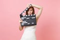 Shocked angry bride woman in wedding dress covering face with classic black film making clapperboard on pastel