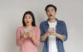 Shocked asian man and woman holding smartphones