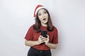 A shocked Asian Santa woman is holding her phone with her mouth wide open isolated by white background. Christmas concept Royalty Free Stock Photo