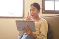A shocked Asian woman is watching a movie on her digital tablet while relaxing on a couch Royalty Free Stock Photo