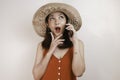 Shocked Asian woman wearing a straw hat talking on a mobile phone and laughing, expressing excitement emotions having a pleasant Royalty Free Stock Photo