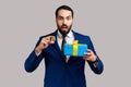 Shocked bearded businessman standing holding present box and golden bitcoin, crypto currency as gift Royalty Free Stock Photo