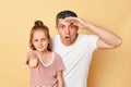 Shocked astonished man looking far with hand near forehead and little kid girl pointing to camera at you standing together Royalty Free Stock Photo