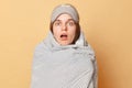 Shocked astonished surprised woman wrapped blanket and wearing sleeping eye mask isolated over beige background waking up lookign