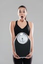 Shocked astonished young woman athlete holding weighing scale