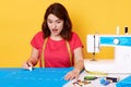 Shocked attractive female opens her mouth widely with surprise, making stitches with chalk on blue piece of fabric, ready to sew