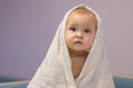 Shocked baby girl covered with towel sits waiting for parent