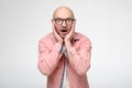 Shocked bald man in glasses emotionally holds hands on his face, in surprise opens mouth and looks into the camera with Royalty Free Stock Photo