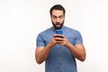 Shocked bearded man looking at smartphone display with big eyes and widely opened mouth, extremely surprised amazed with bonuses