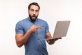 Shocked bearded man pointing finger at laptop he holding and looking at camera with opened mouth and big eyes, astonishment Royalty Free Stock Photo