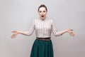 Shocked beautiful young woman in striped shirt and green skirt with collected ban hairstyle, standing with raised arms and looking Royalty Free Stock Photo