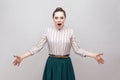 Shocked beautiful young woman in striped shirt and green skirt with collected ban hairstyle, standing with raised arms and looking Royalty Free Stock Photo