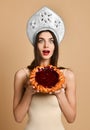 Shocked beauty russian woman in kokoshnik hat, has cake during dinner time, being surprised