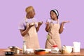 Shocked black guy holding dough and his ignorant girlfriend shrugging shoulders on violet studio background