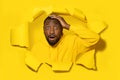 Shocked black man touching his head and looking through hole in yellow paper, free space Royalty Free Stock Photo