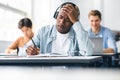 Shocked black student writing test sitting at desk in class