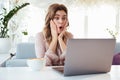 Shocked blondy woman in blouse sitting by the table