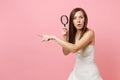 Shocked bride woman in white wedding dress pointing index finger aside and holding magnifying glass on pastel