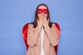 Shocked brown haired woman wearing superhero costume posing over blue background making mistake covering mouth with hands