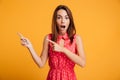 Shocked brunette woman in dress winks and pointing up