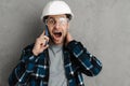 Shocked builder man in helmet and goggles talking on mobile phone Royalty Free Stock Photo