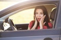 Shocked Caucasian female with astonished expression, holds hands on cheeks, poses in luxury car, being surprised to forget driving