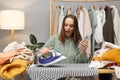 Shocked Caucasian woman with brown hair ironing clothing while sitting in her wardrobe at home burning hole in her shirt while