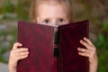 Shocked child holding book in her hands, looking at camera. Emotions of schoolgirl reading book. Knowledge and learning Royalty Free Stock Photo