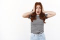 Shocked concerned young ambushed redhead woman in striped t-shirt, hold hands on head, furrow eyebrows nervously, open Royalty Free Stock Photo