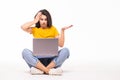 Shocked confused woman in t-shirt sitting on the floor with laptop computer over white background