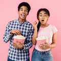 Shocked couple eating popcorn over pink background