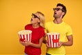 Shocked couple friends man and woman in red and yellow t-shirts 3d glasses isolated on yellow background. People in cinema,