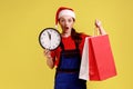 Shocked courier female showing wall clock and shopping bags, delivery Christmas in time.