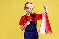 Shocked delivery woman holding pointing at shopping bags, offering free shipping from fashion store.