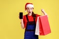 Shocked delivery woman holding shopping bags and showing smart phone with empty display