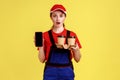 Shocked delivery woman holding take away coffee, showing mobile phone with blank screen.