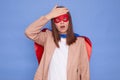 Shocked despair brown haired woman wearing superhero costume posing isolated over blue background having problems showing facepalm