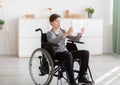 Shocked disabled teen boy in wheelchair using tablet pc at home, browsing internet or watching cool video online Royalty Free Stock Photo