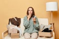 Shocked displeased woman wearing knitted sweater sitting on sofa among carton box using mobile phone realizing she make wrong