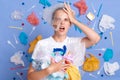 Shocked displeased woman wearing white shirt isolated on blue wall with garbage around frowning face being unhappy clean up trash