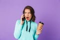 Shocked displeased young woman posing isolated over purple background wall talking by mobile phone