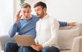 Shocked elderly man and adult son using laptop sitting indoor