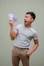 Shocked and excited Asian man holding USD dollar bills, standing against a green studio background
