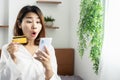 Shocked female Asian customer holding credit card shopping online with mobile phone surprised with a promotion