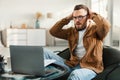 Shocked Freelancer Man Looking At Laptop Touching Head At Home