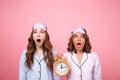 Shocked friends women in pajamas holding alarm clock