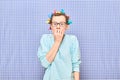 Shocked frightened girl with bright hair curlers is biting nails