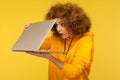 Shocked frightened woman with curly hair in urban style hoody looking furtively at half closed laptop screen Royalty Free Stock Photo