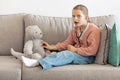 Shocked funny caucasian little girl playing doctor with toy bear, listens to breath with stethoscope Royalty Free Stock Photo