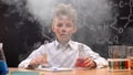 Shocked funny dirty schoolboy holding chemical tube and flask, smoke around him